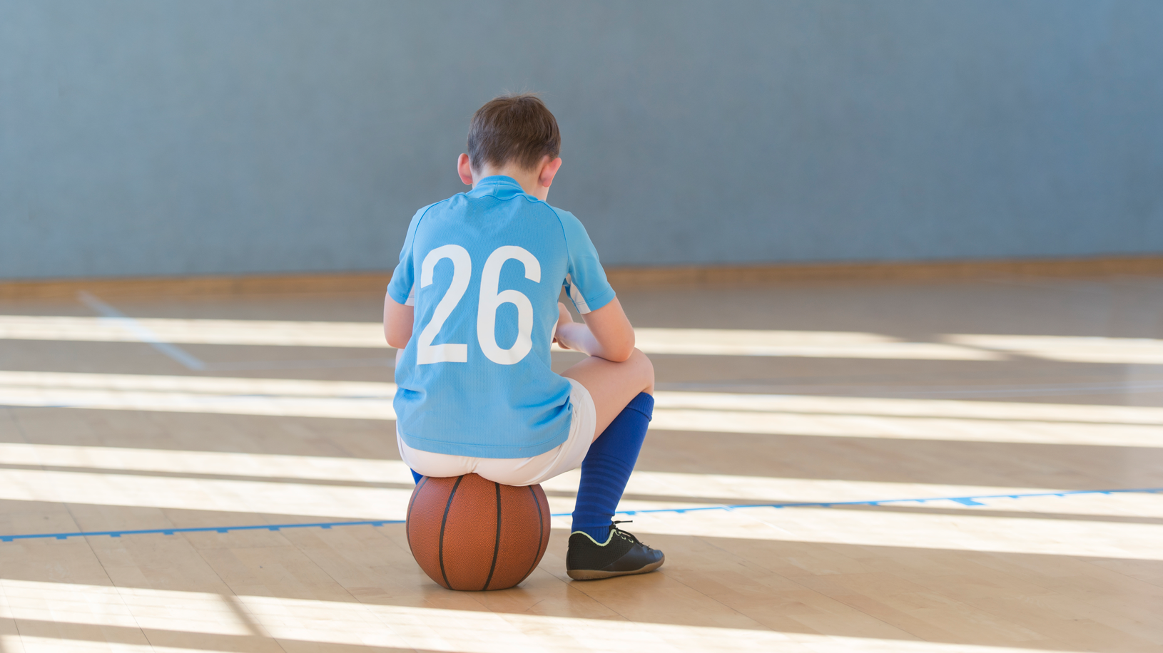 Rear view of boy wearing a jersey and other sports attire and sitting on a ball