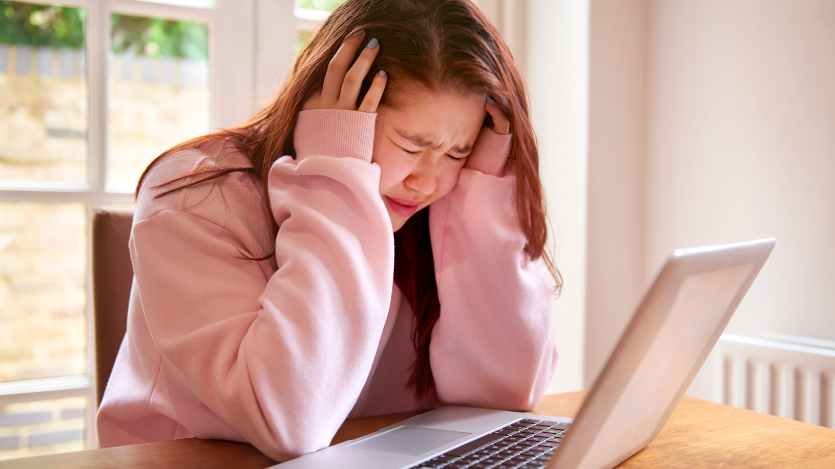 Distraught girl with eyes closed sitting in front of laptop