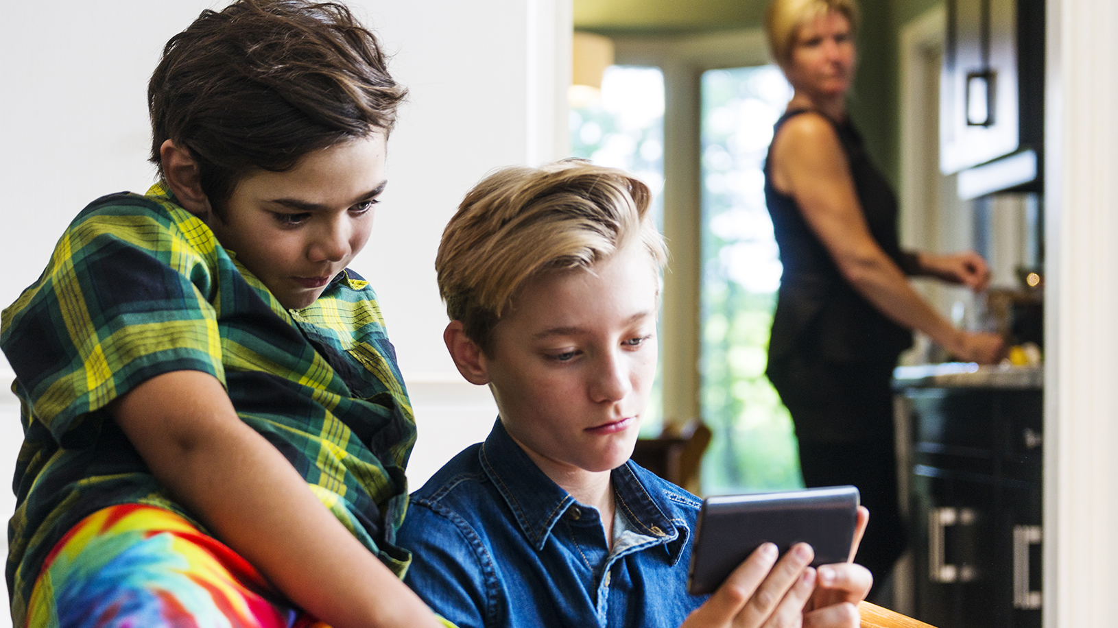 Two children looking at phone with concerned caregiver in background