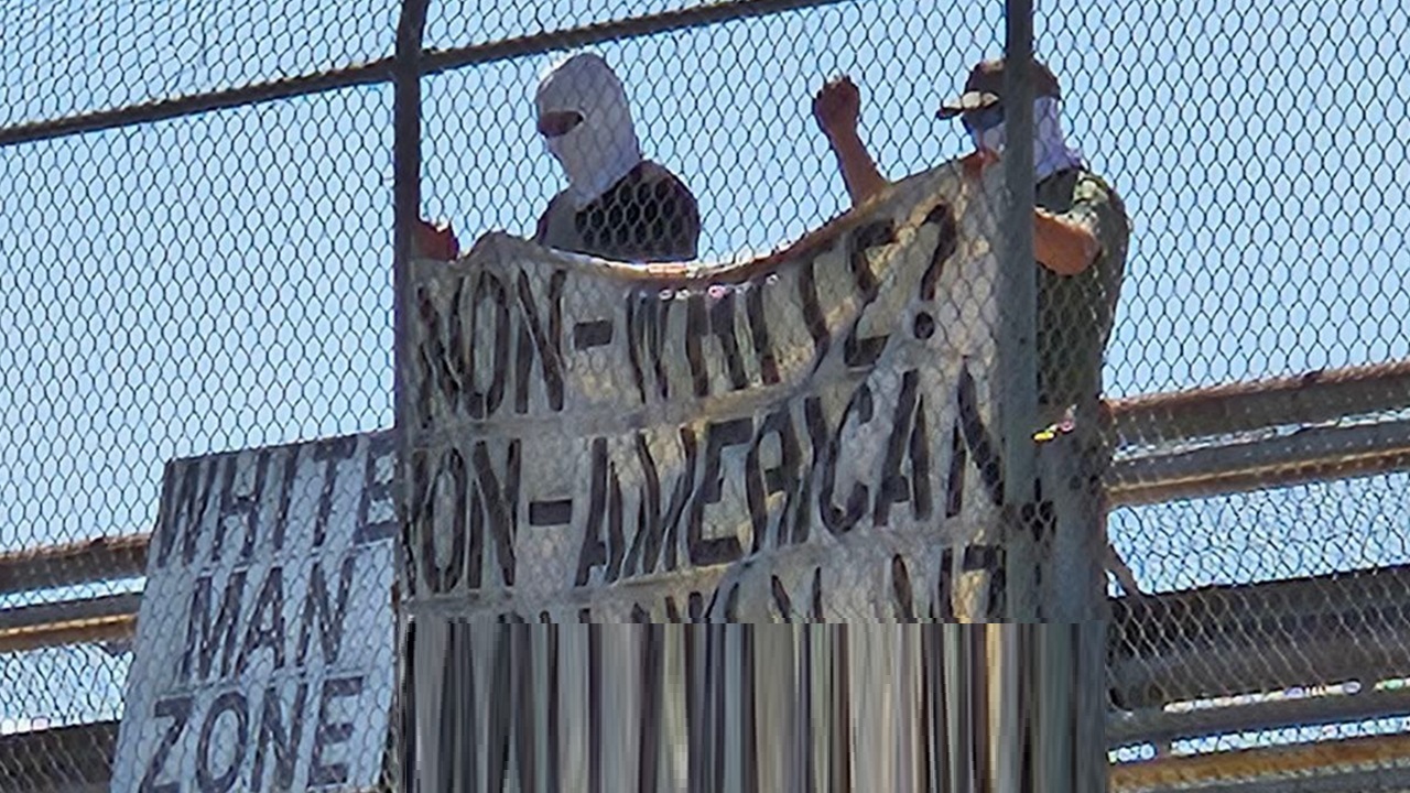 An image of two individuals associated with White Lives Matter Montana demonstrating on an overpass display a sign that reads, “white man zone” and a banner which reads: “Non-white? Non-American.”