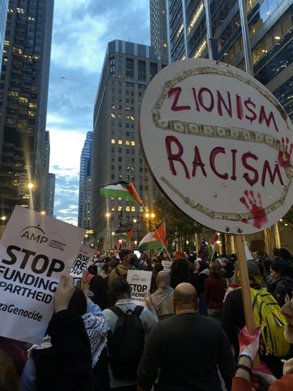 An image of an antisemitic sign at an AMP-sponsored anti-Israel rally in Chicago, October 2023 depicting dollar bills in the shape of a snake, bloody handprints and the message “Zionism is racism” with the letter “s” stylized as a dollar sign. 