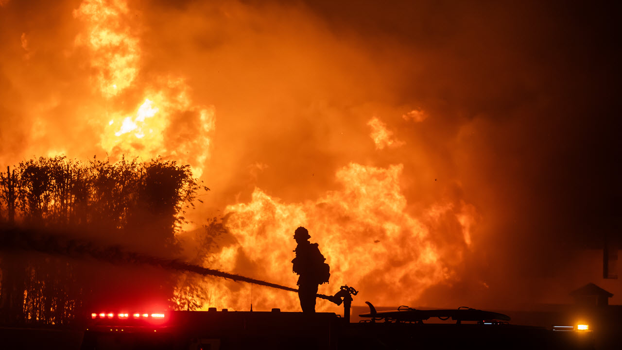 A firefighter stands on top of a fire truck to battle the Palisades Fire while it burns homes on the Pacific Coast Highway amid a powerful windstorm on January 8, 2025 in Los Angeles, California. (Apu Gomes/Getty Images)