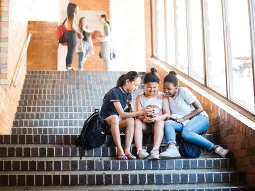 Friends Using Mobile Phone on Steps in High School